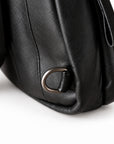 Close-up of a black leather bag corner showing a dark metal D-ring attachment and part of the strap.