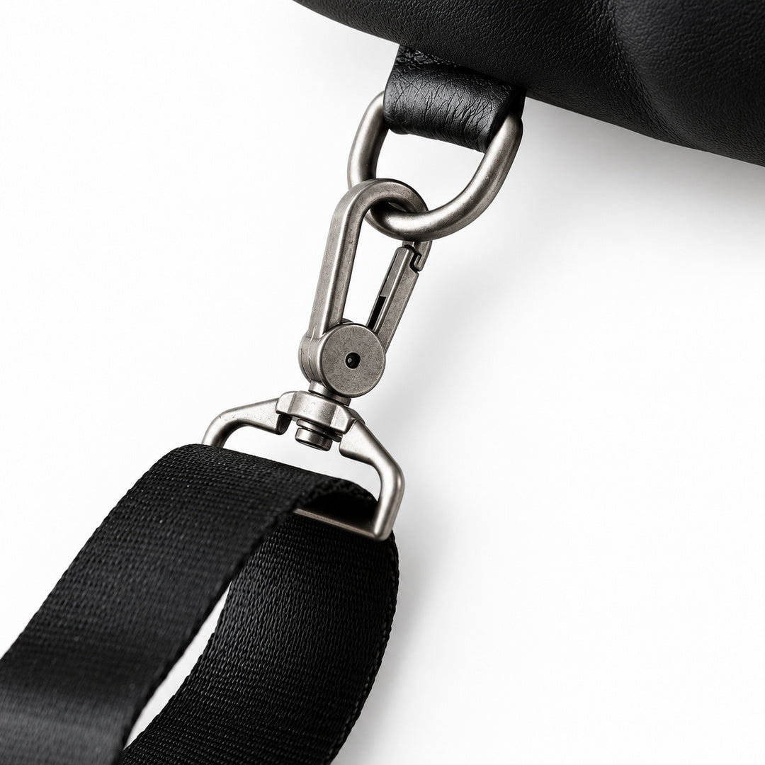 Close-up of a black bag strap with a black leather section and a black woven strap, attached to a silver metal swivel clasp.