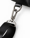 Close-up of a black bag strap with a black leather section and a black woven strap, attached to a silver metal swivel clasp.