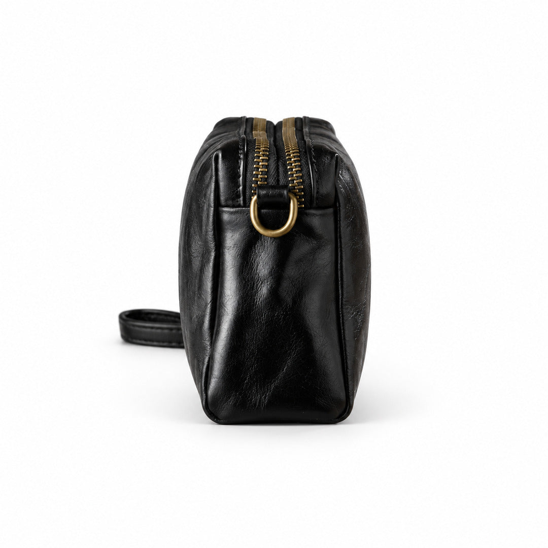 Black leather crossbody bag with gold-tone hardware, shown from the side profile.