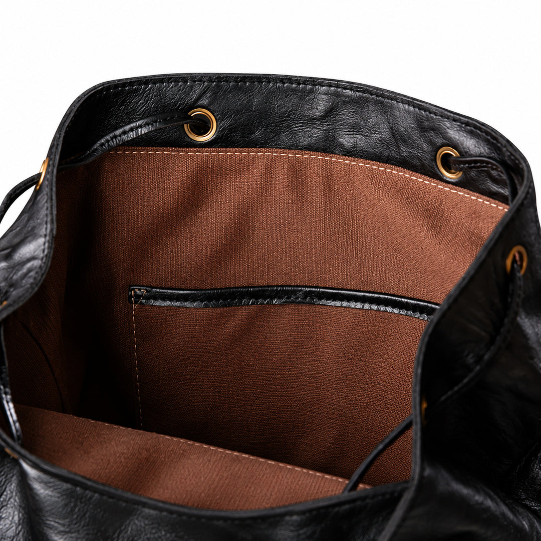Close-up of the interior of a black leather bag, showing a brown fabric lining with a front slip pocket and gold-tone grommets.