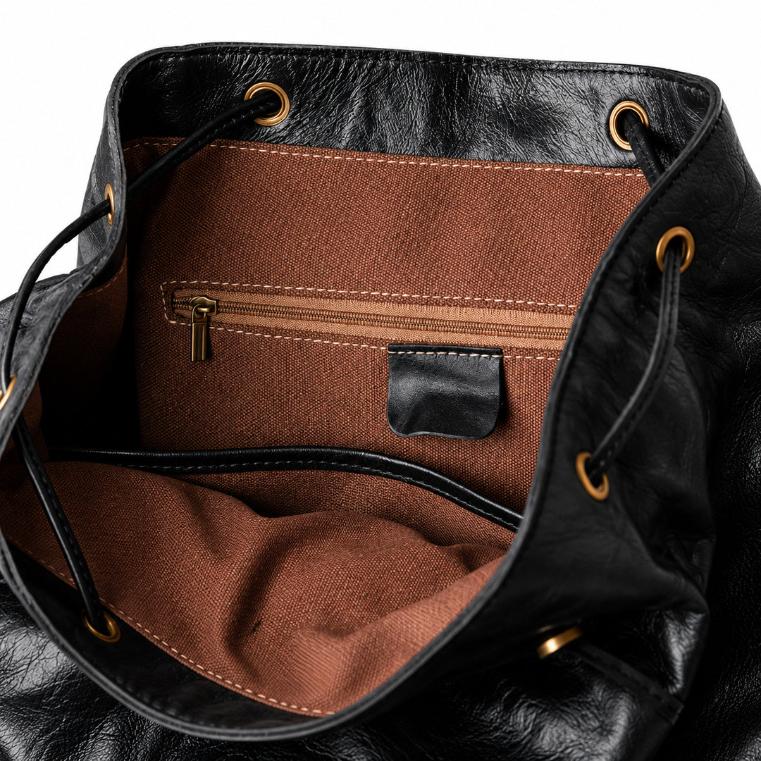 Close-up of the interior of a black leather bag with a brown fabric lining, showing a zippered pocket, stitched interior, and gold-tone grommets.