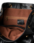 Close-up of the interior of a black leather bag with a brown fabric lining, showing a zippered pocket, stitched interior, and gold-tone grommets.