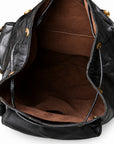 Close-up of the interior of a black leather handbag with a brown fabric lining and gold-tone hardware, shown against a white background.