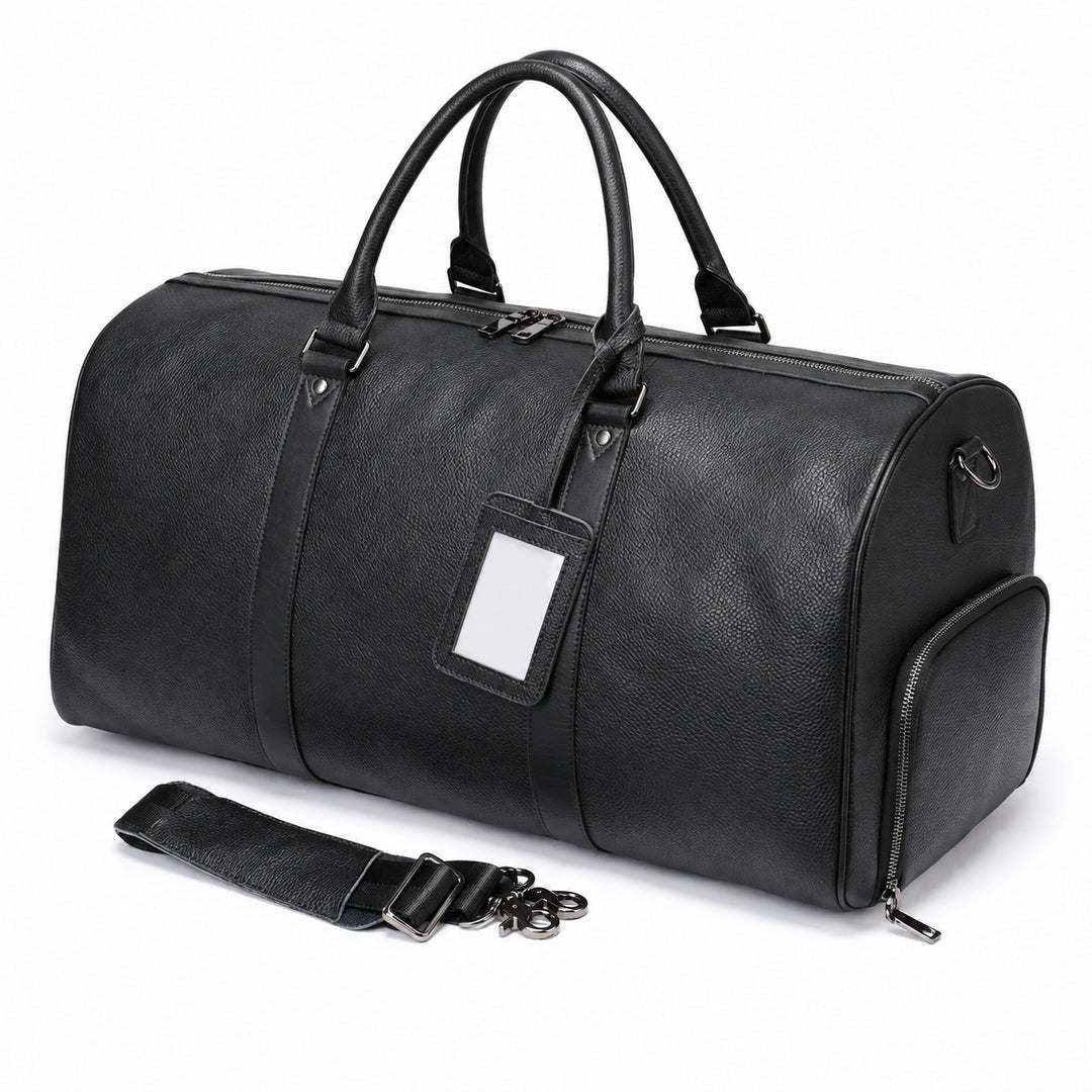 A black pebbled leather duffel bag with dual top handles, a zippered main compartment, a side pocket, a detachable shoulder strap, and a blank white luggage tag, shown on a white background.