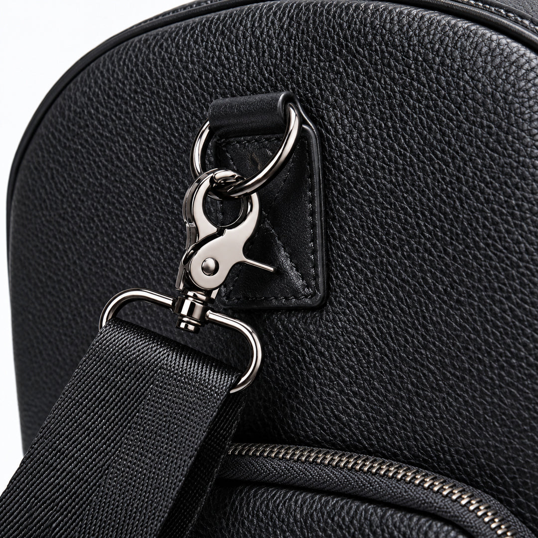 Close-up of a black pebbled leather bag with a black webbing strap attached via silver metal rings and a snap hook clasp, with a zipper visible below.