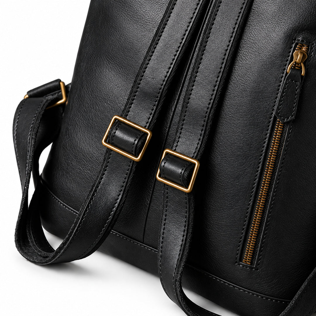 Close-up of a black faux-leather shoulder bag with gold-tone hardware, showing a side zipper, buckle straps, and part of the strap.
