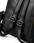 Close-up of a black faux-leather shoulder bag with gold-tone hardware, showing a side zipper, buckle straps, and part of the strap.