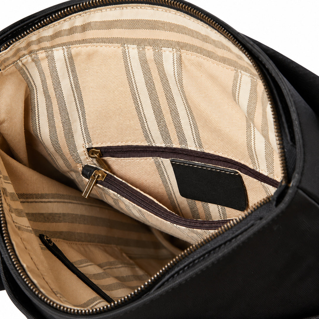 Close-up of the interior of a black bag, showing a beige and brown striped lining with a zippered pocket and gold-tone zipper hardware.