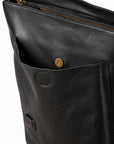 Close-up of a black leather bag showing a front pocket with a brass snap button, a zipper opening at the top, and a small leather tag near the bottom.