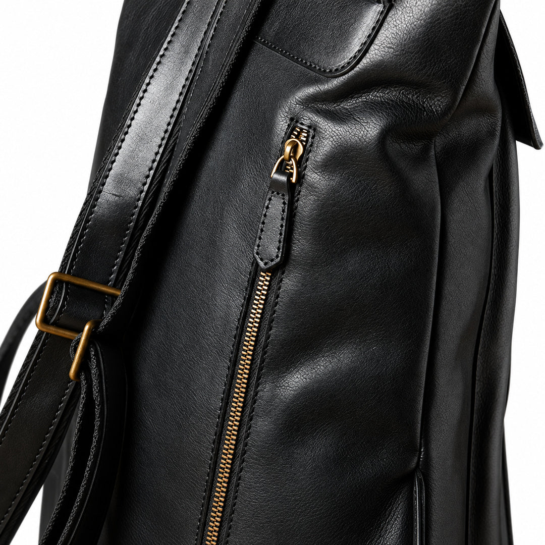 Close-up of a black leather bag showing a vertical zippered pocket with a gold-tone zipper pull and a matching gold buckle on the shoulder strap.