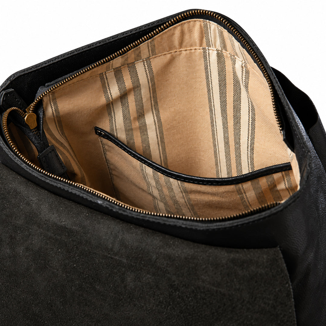 Close-up of the interior of a black leather bag, showing a tan and beige striped fabric lining with a zippered pocket.