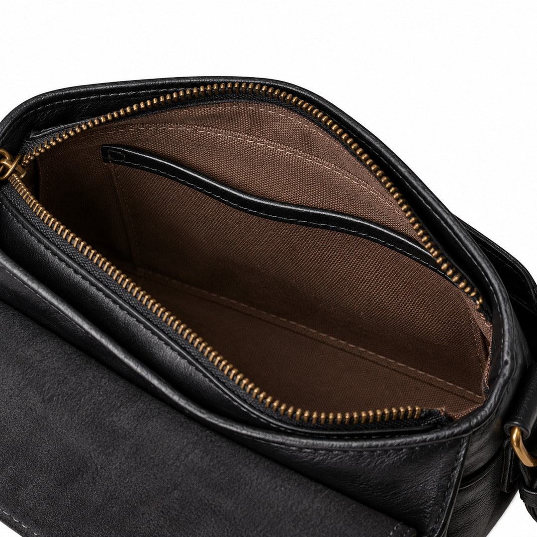 Close-up of the interior of a black leather bag, showing a brown fabric lining with a zippered compartment and gold-tone zipper teeth.