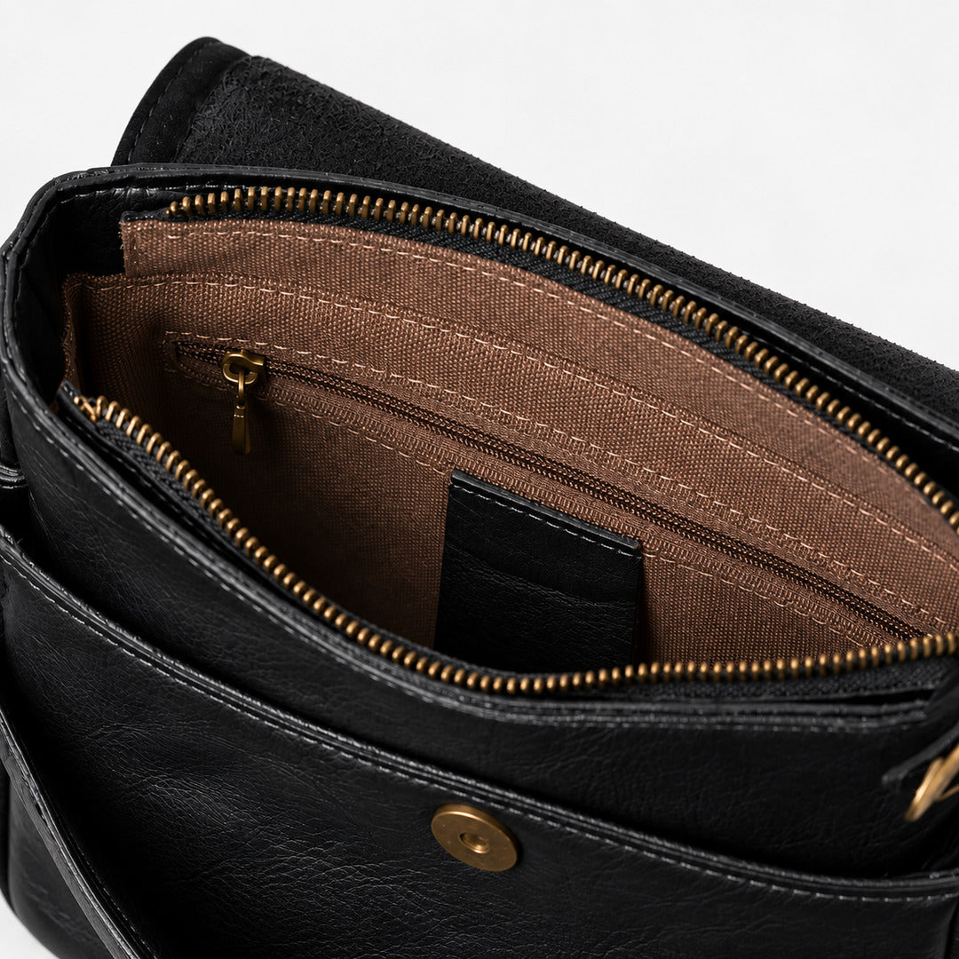 Close-up of the interior of a black leather bag, showing a brown fabric-lined compartment with gold-tone zippers and hardware.