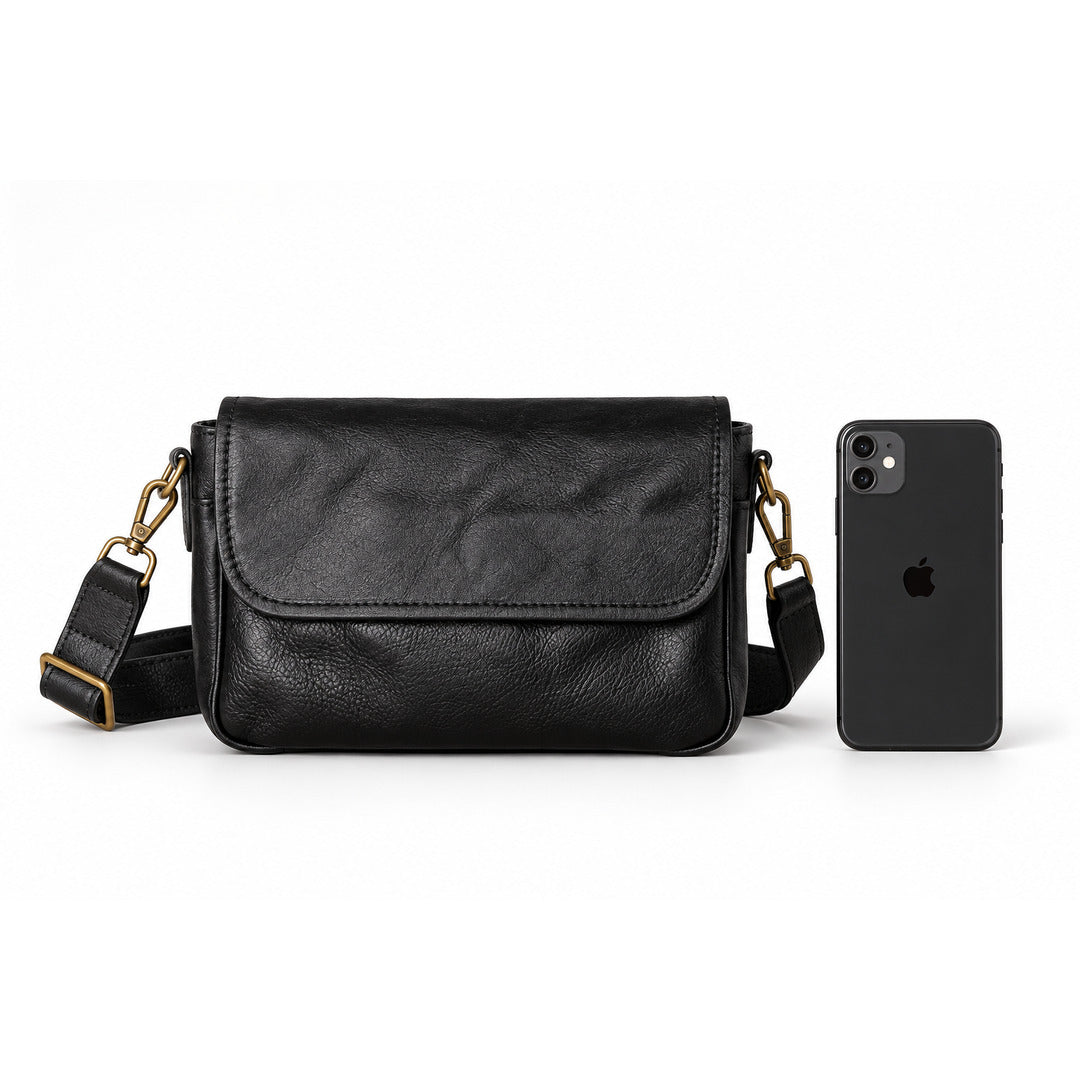 A black leather crossbody bag with gold-tone hardware, shown next to a black smartphone for scale.