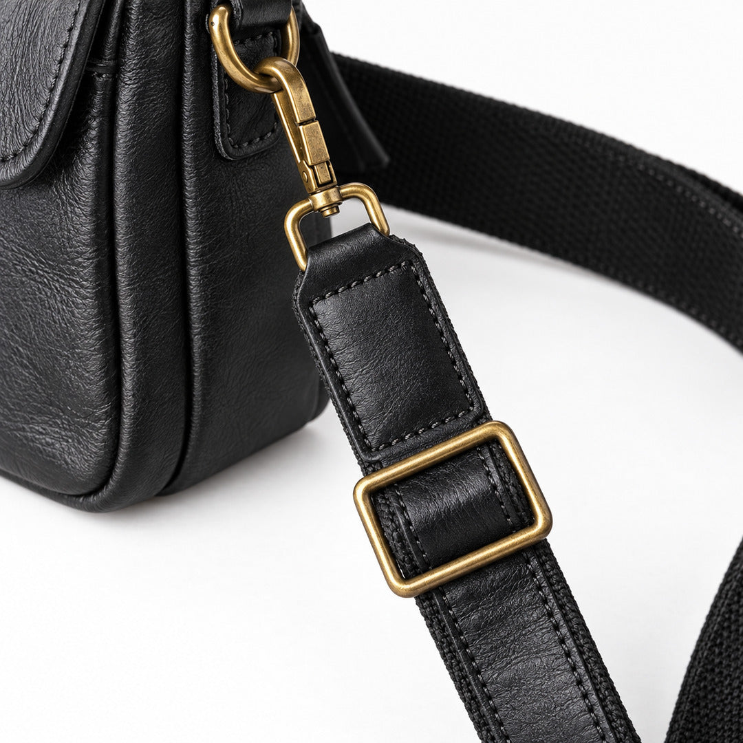 Close-up of a black leather bag strap with a gold-tone metal buckle and clasp, attached to a black textured bag.