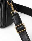 Close-up of a black leather bag strap with a gold-tone metal buckle and clasp, attached to a black textured bag.