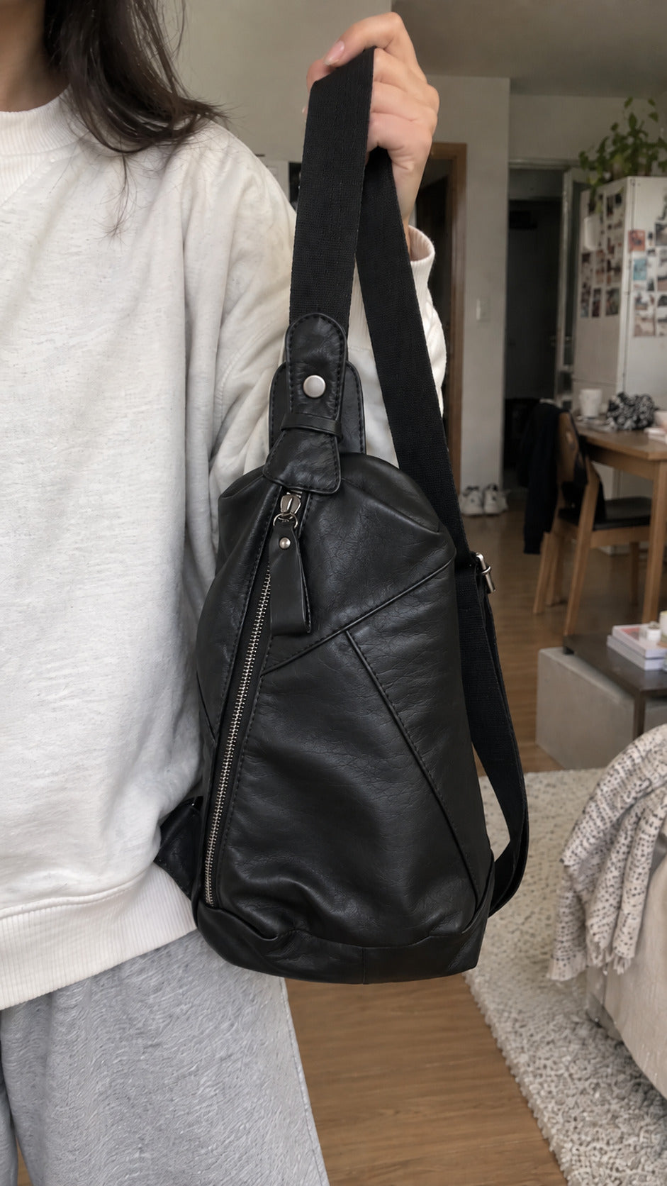 Woman holding a black leather-look sling bag with adjustable shoulder strap and front zipper