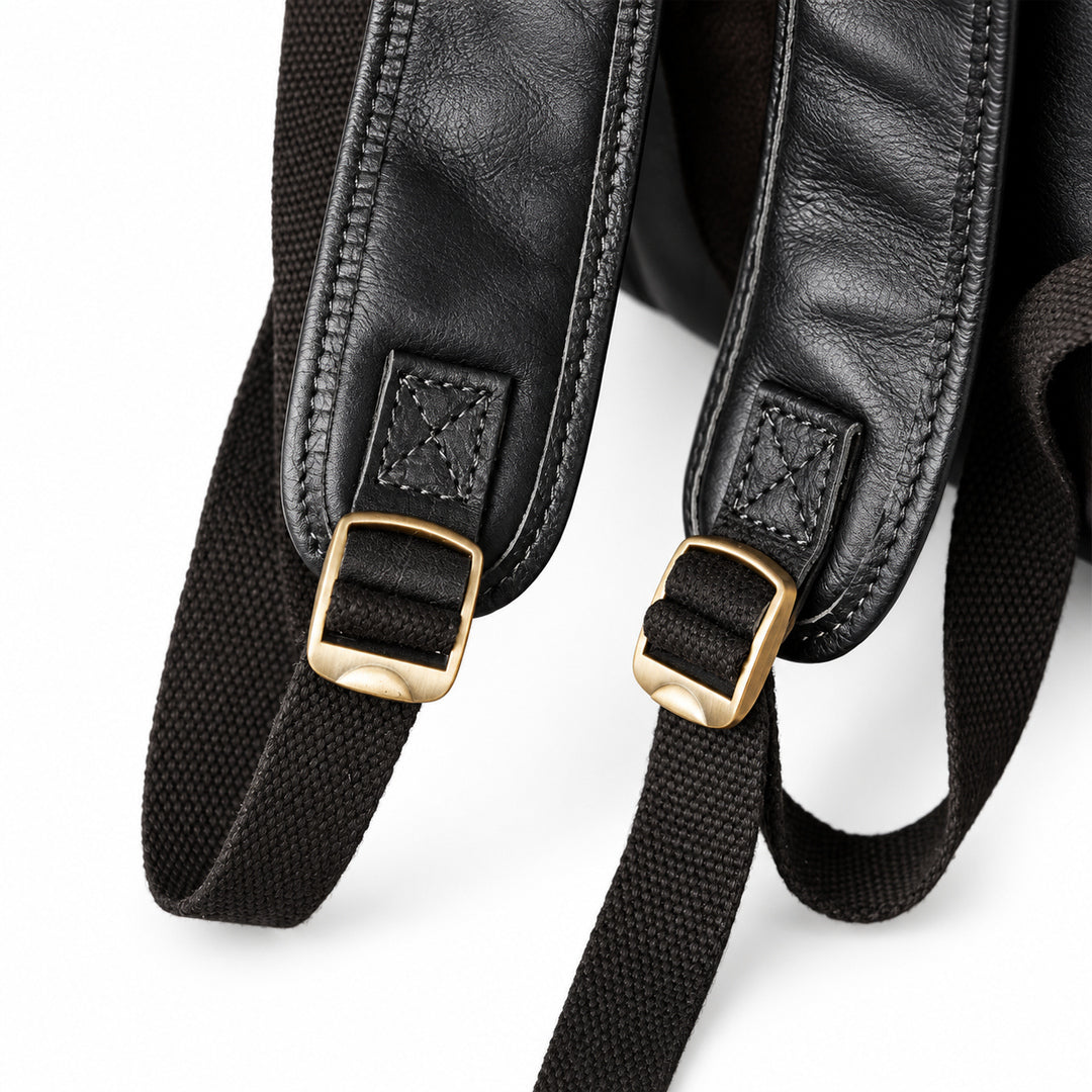Close-up of a black leather and canvas backpack strap with gold-tone metal buckles.