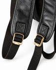 Close-up of a black leather and canvas backpack strap with gold-tone metal buckles.