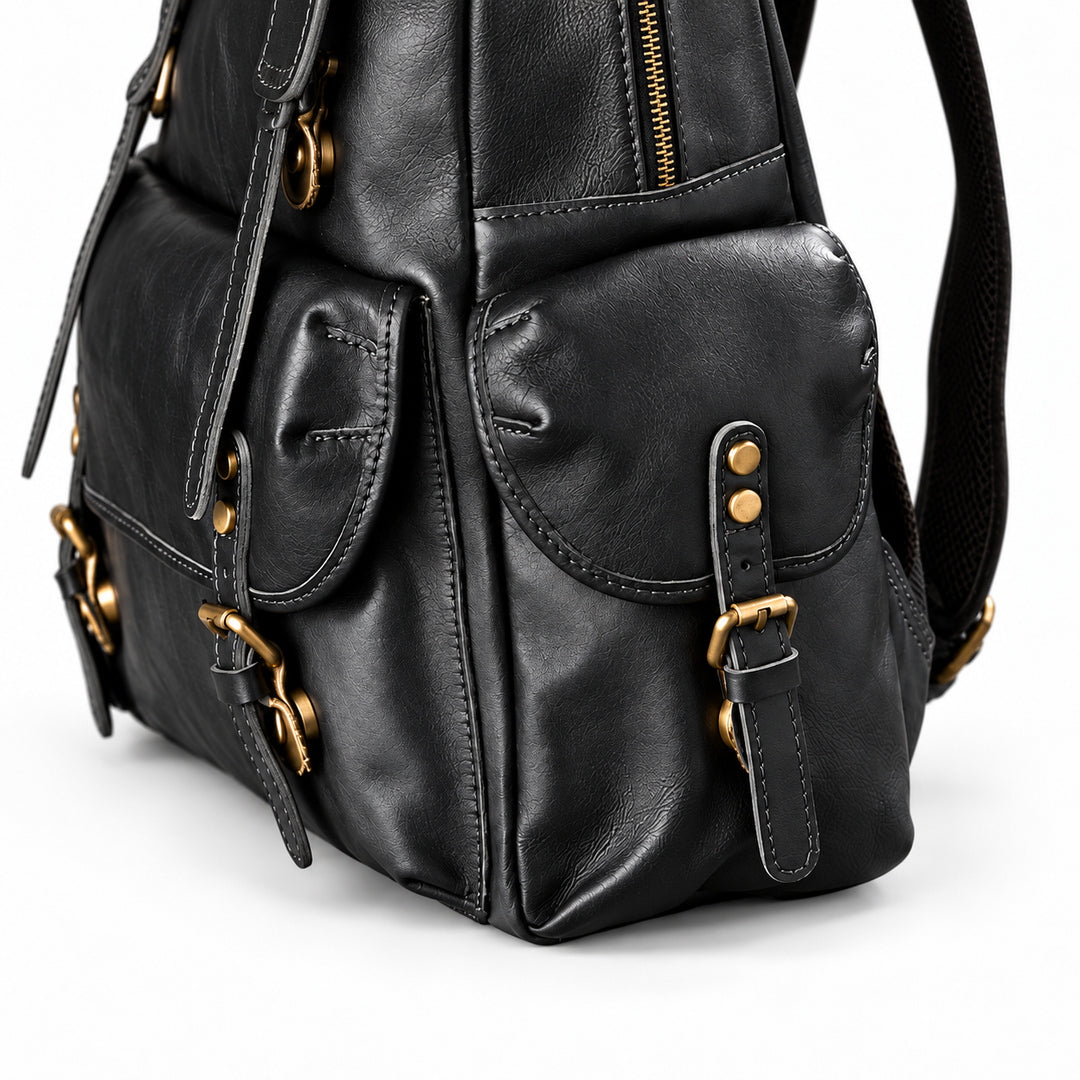 Close-up of a black leather backpack with gold-tone hardware, showing front flap pockets, buckle straps, and a zipper.