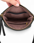 A close-up of a black leather crossbody bag being held open by a hand, showing a brown fabric interior with gold-tone zippers and a small zip pocket.