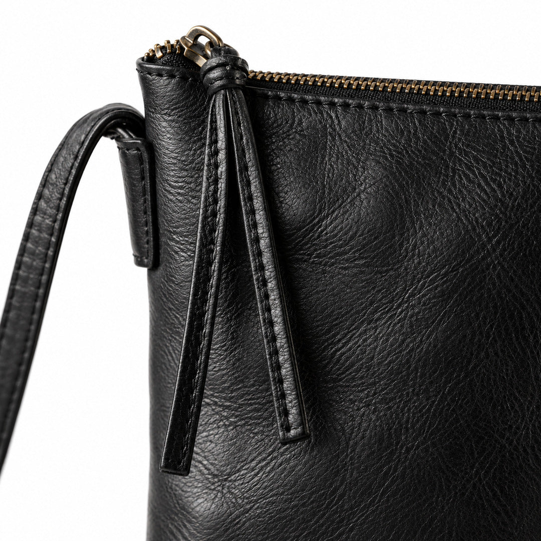 Close-up of a black textured leather clutch or zip pouch with a gold-tone zipper and a leather tassel detail, shown on a white background.