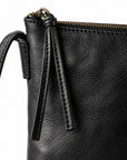 Close-up of a black textured leather clutch or zip pouch with a gold-tone zipper and a leather tassel detail, shown on a white background.