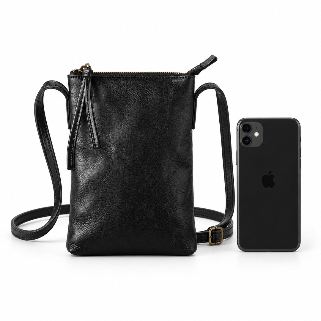 Black leather crossbody phone bag with a top zipper, shown next to a black smartphone for scale on a white background.
