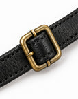 A close-up of a black textured leather strap with a square antique bronze buckle, shown on a clean white background.