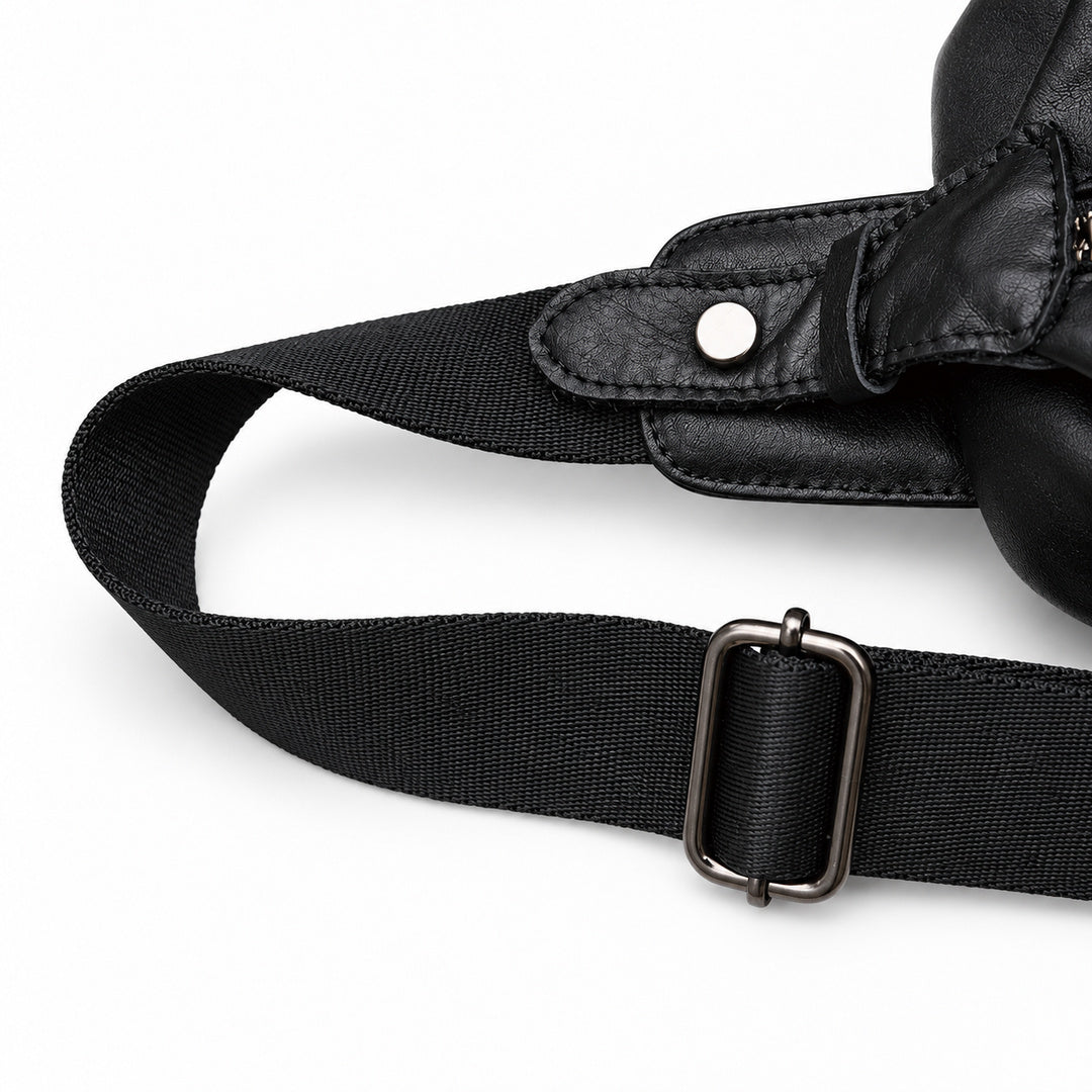 Close-up of the sling bag's black woven shoulder strap, metal adjustment buckle and leather snap attachment.