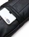Close-up of a silver smartphone partially tucked into the black leather sling bag's rear slip pocket.