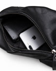 Open main compartment of a black leather sling bag holding a smartphone and black wallet.