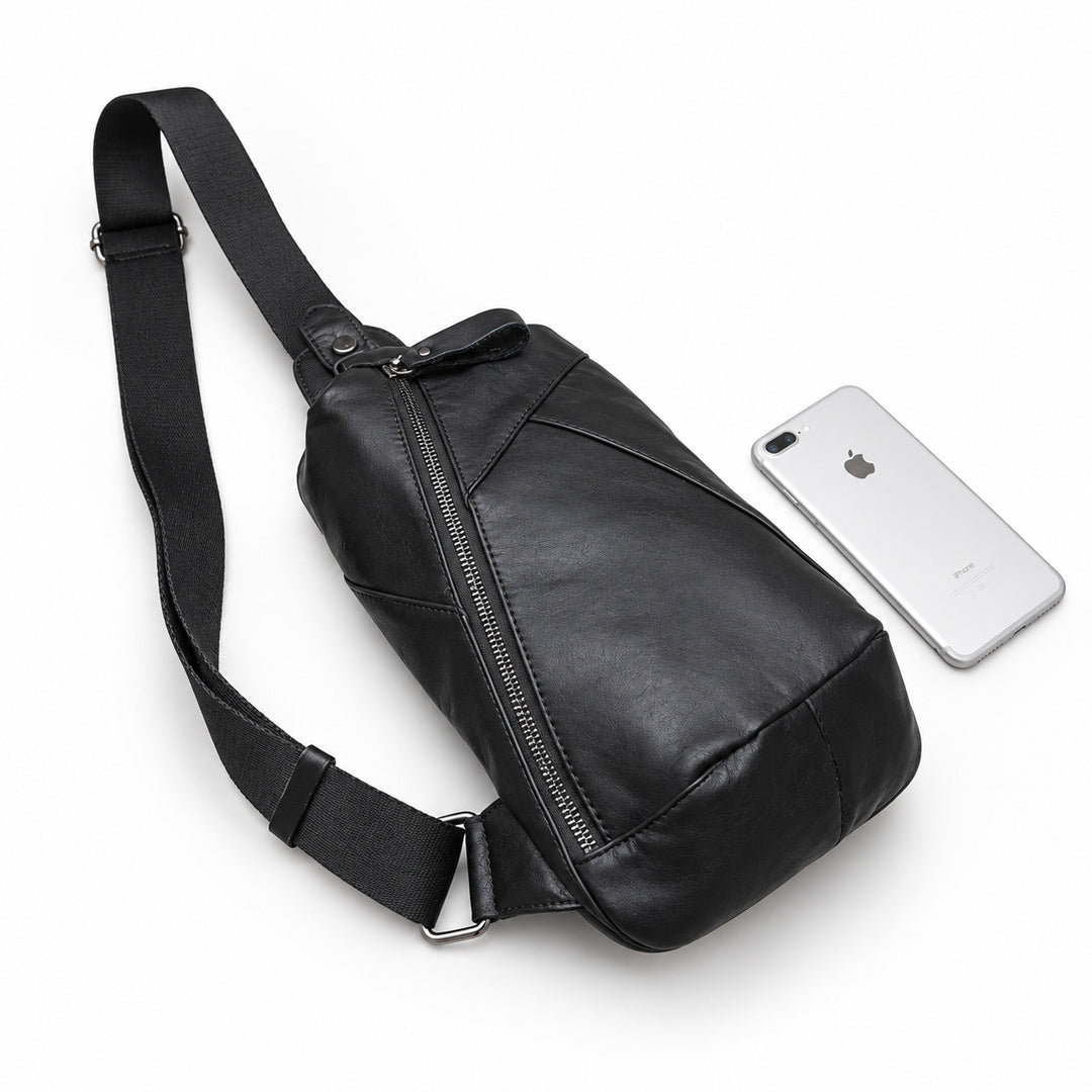 Black leather sling bag lying beside a silver smartphone for size comparison.