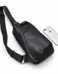 Black leather sling bag lying beside a silver smartphone for size comparison.