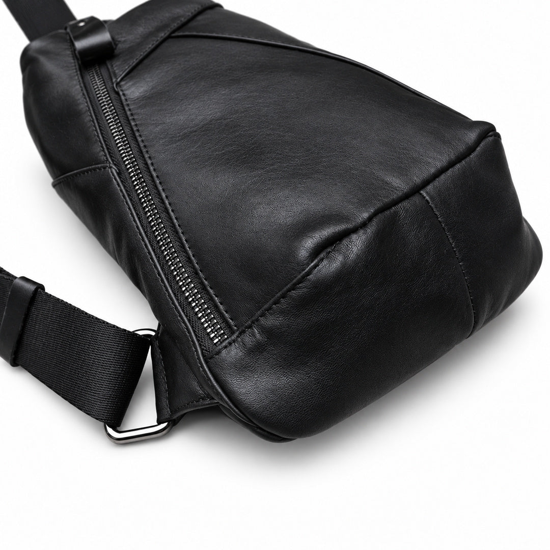 Close-up of a black leather sling bag showing the leather texture, zipper, stitching and lower strap attachment.