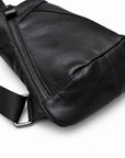 Close-up of a black leather sling bag showing the leather texture, zipper, stitching and lower strap attachment.