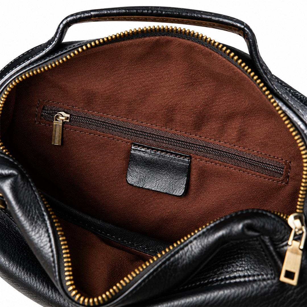 Close-up of the interior of a black leather handbag, showing a brown fabric lining with a horizontal zippered pocket and gold-tone zipper hardware.