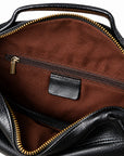 Close-up of the interior of a black leather handbag, showing a brown fabric lining with a horizontal zippered pocket and gold-tone zipper hardware.
