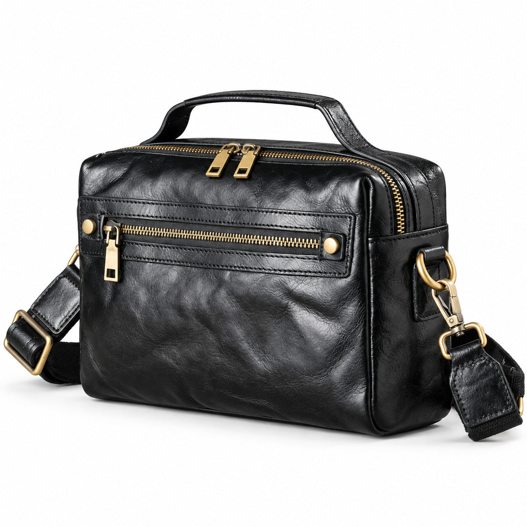 Black leather crossbody bag with gold-tone hardware, featuring a top handle, a front zippered pocket, and an adjustable shoulder strap.