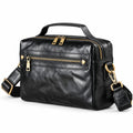 Black leather crossbody bag with gold-tone hardware, featuring a top handle, a front zippered pocket, and an adjustable shoulder strap.