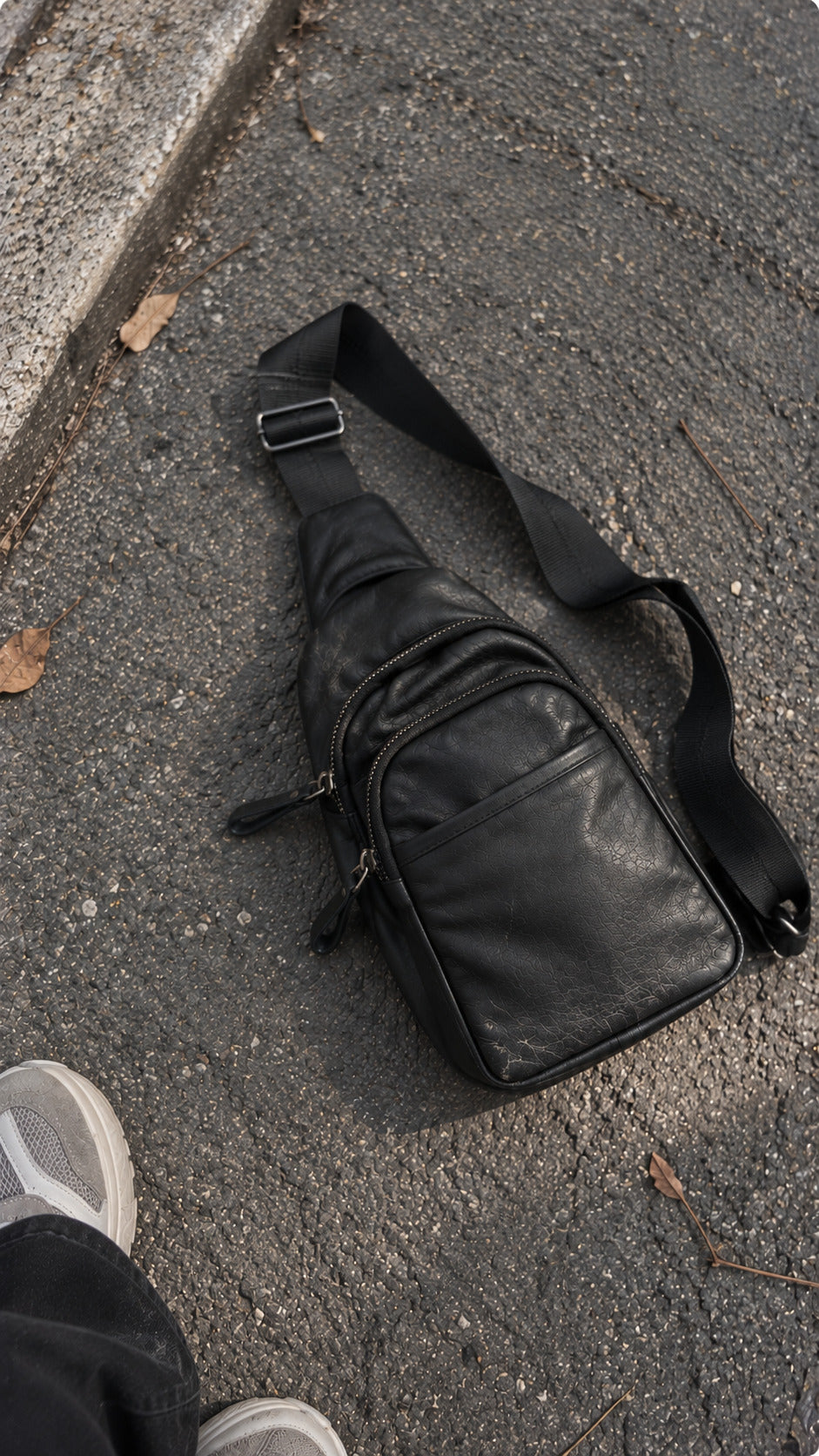 Black leather-look sling bag with multiple zipper compartments and adjustable shoulder strap