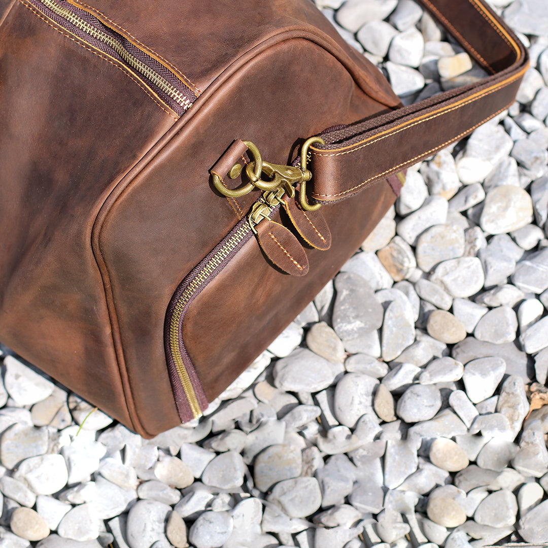 Close-up of brass zippers and details on the side pocket of a premium leather duffle bag.