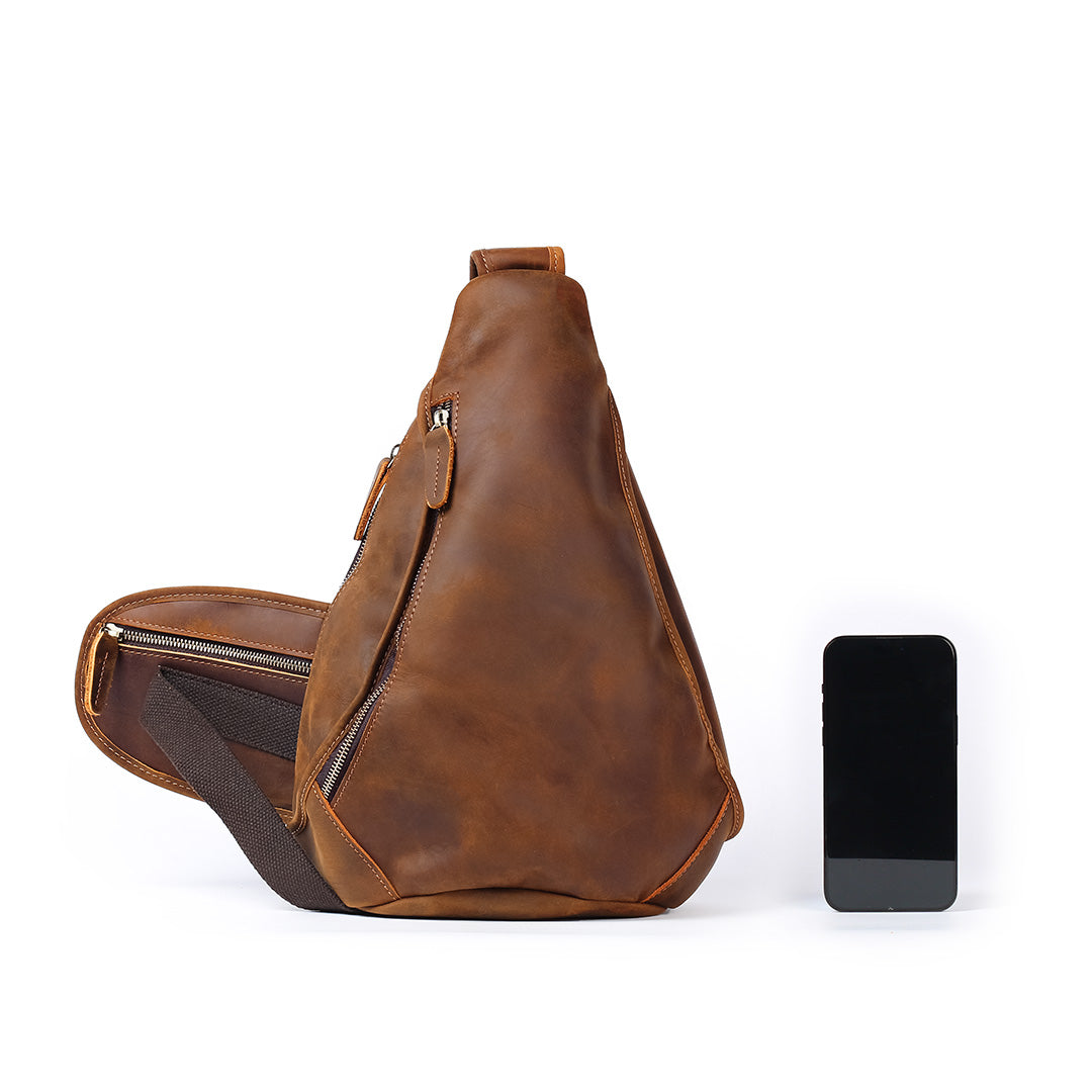 Brown leather sling bag next to a smartphone on a white background