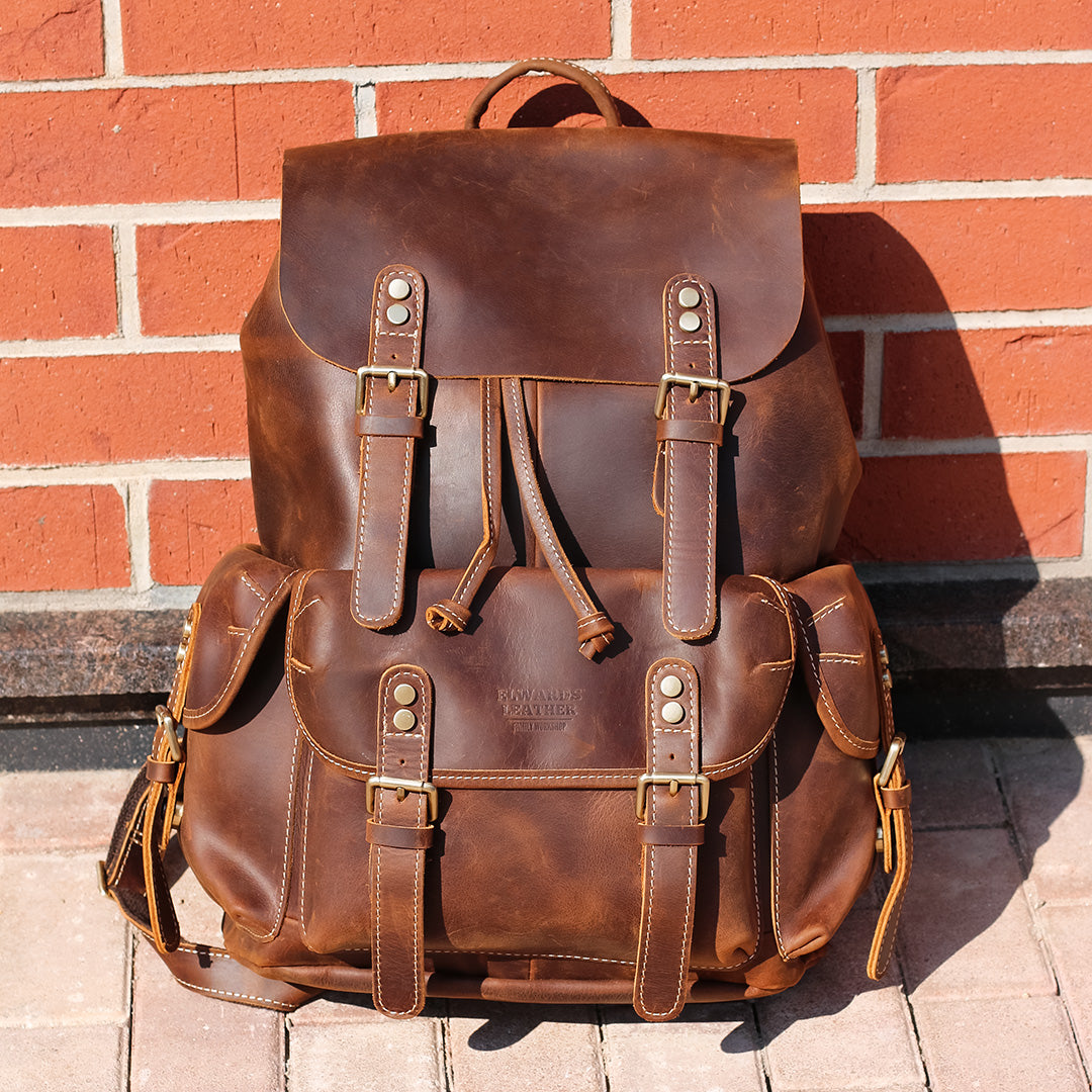 Brown leather backpack against a brick wall