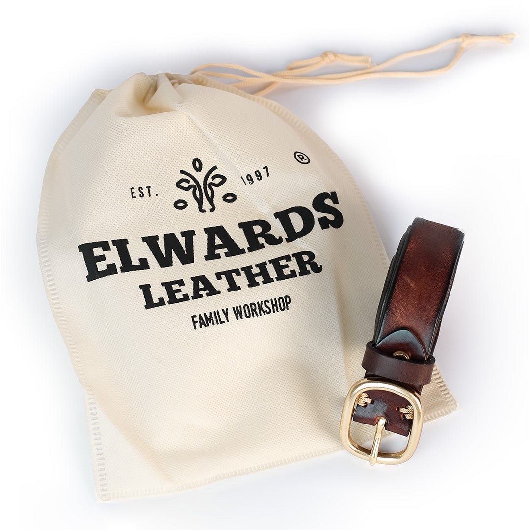 Brown leather belt with gold buckle on a branded drawstring bag against a white background