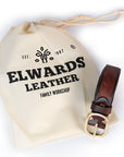 Brown leather belt with gold buckle on a branded drawstring bag against a white background