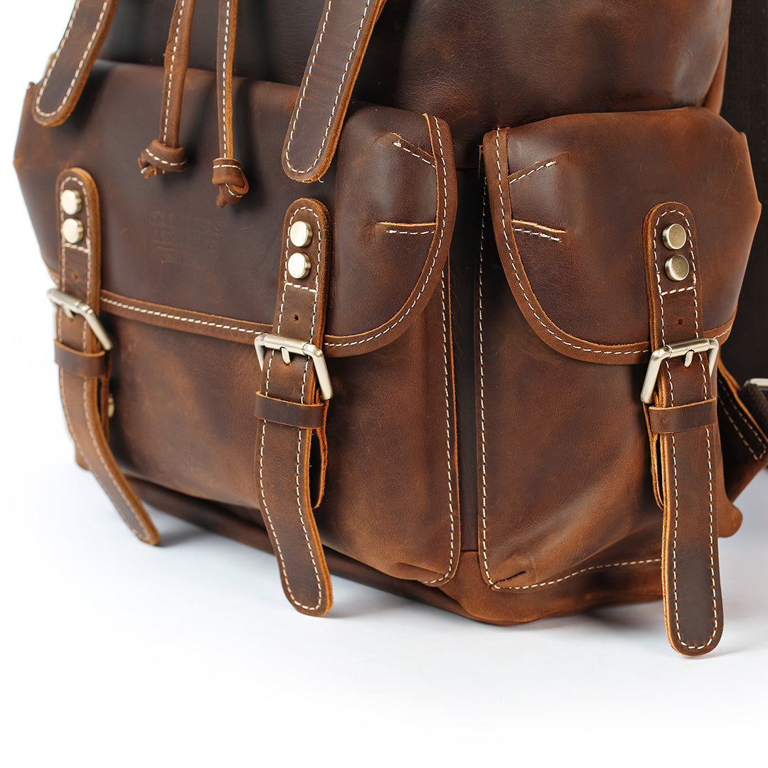 Close-up of a brown leather backpack with gold buckles on a white background