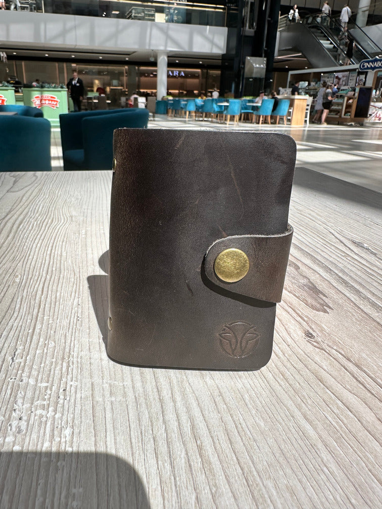 Brown handmade leather card holder displayed on a table, emphasizing its luxurious design and button clasp.