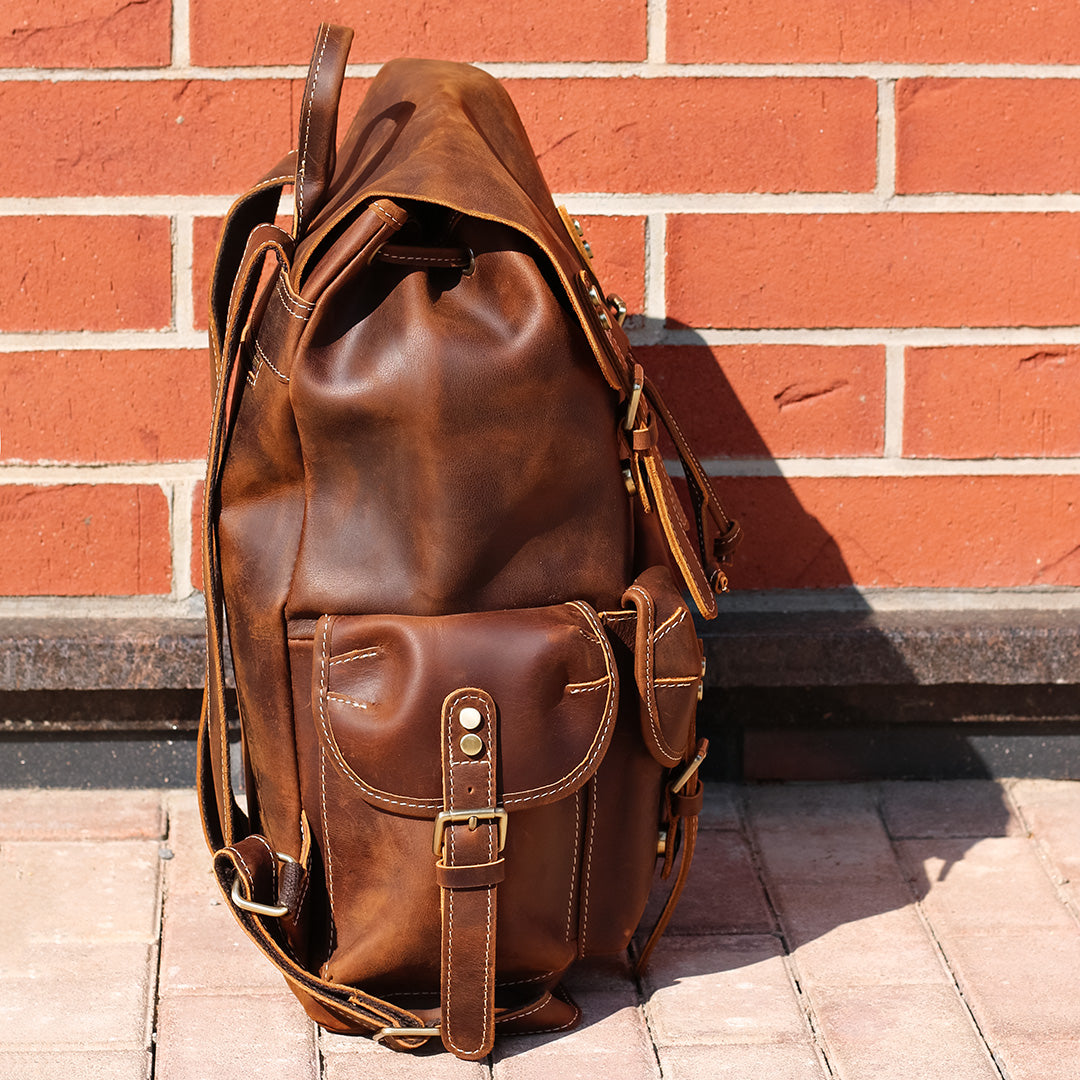 Brown leather backpack against a brick wall
